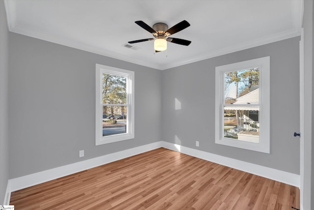 empty room with light wood finished floors, baseboards, visible vents, and crown molding