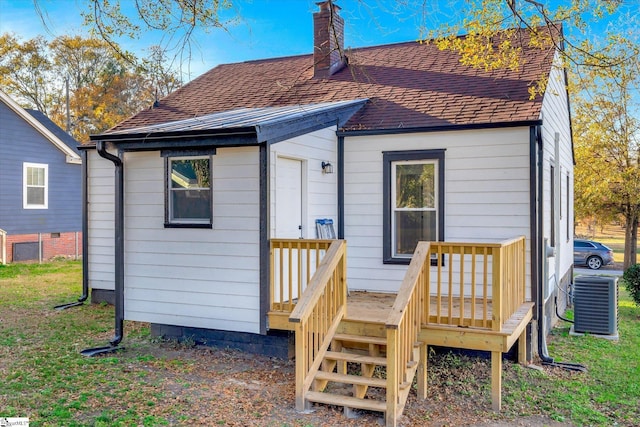 back of house with central AC unit, a chimney, and a shingled roof