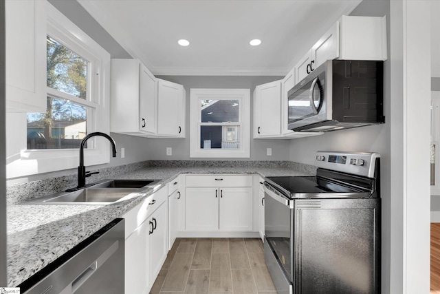 kitchen with stainless steel appliances, white cabinetry, a sink, and light stone countertops