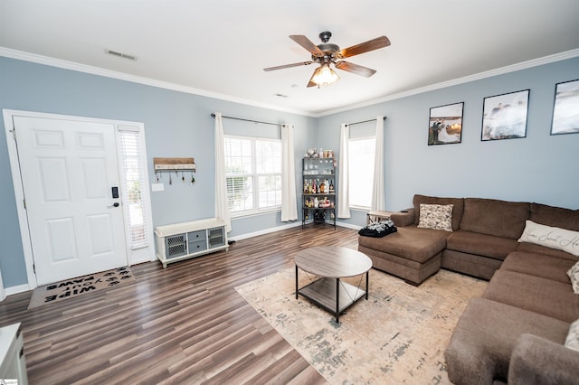 living area with ornamental molding, wood finished floors, visible vents, and baseboards