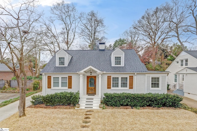 new england style home featuring a shingled roof, brick siding, fence, and a chimney