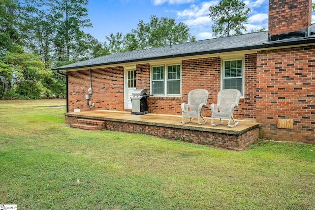 exterior space with a shingled roof, a lawn, a chimney, a patio area, and brick siding