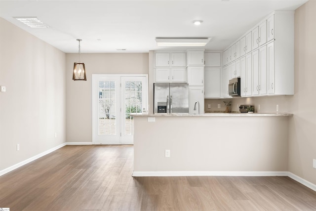 kitchen with white cabinets, light wood-style flooring, appliances with stainless steel finishes, hanging light fixtures, and a peninsula