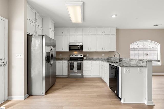 kitchen featuring a peninsula, a sink, white cabinetry, appliances with stainless steel finishes, and light stone countertops