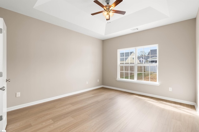 spare room with a ceiling fan, visible vents, baseboards, light wood-type flooring, and a raised ceiling