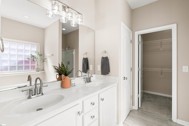 full bathroom with double vanity, a shower stall, a walk in closet, and a sink