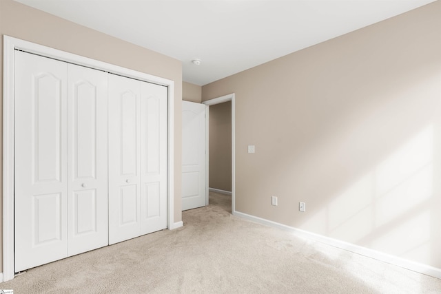 unfurnished bedroom with light carpet, a closet, and baseboards