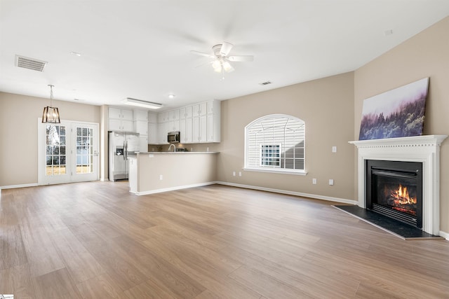 unfurnished living room featuring light wood-style floors, visible vents, a ceiling fan, and a glass covered fireplace