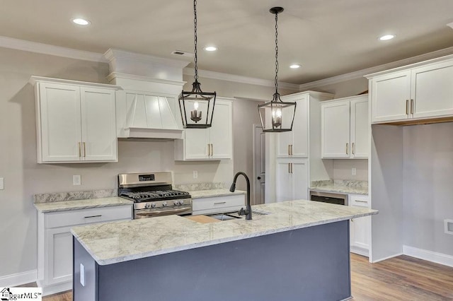 kitchen with stainless steel range with gas stovetop, a sink, white cabinets, an island with sink, and decorative light fixtures