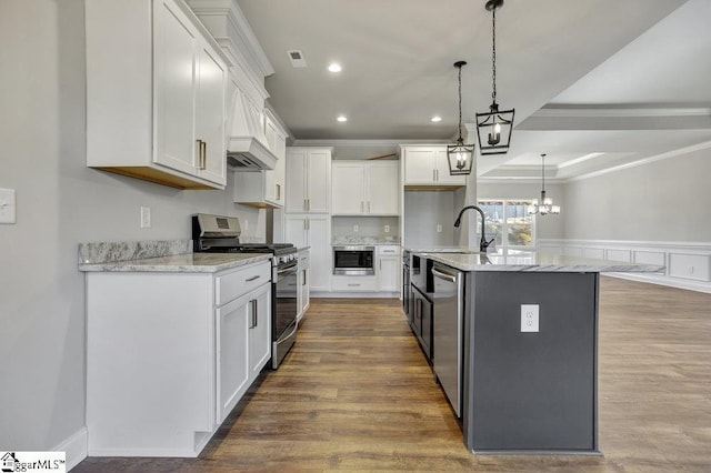 kitchen featuring a center island with sink, white cabinets, appliances with stainless steel finishes, hanging light fixtures, and a sink