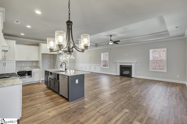 kitchen featuring a center island with sink, white cabinets, open floor plan, hanging light fixtures, and a tray ceiling