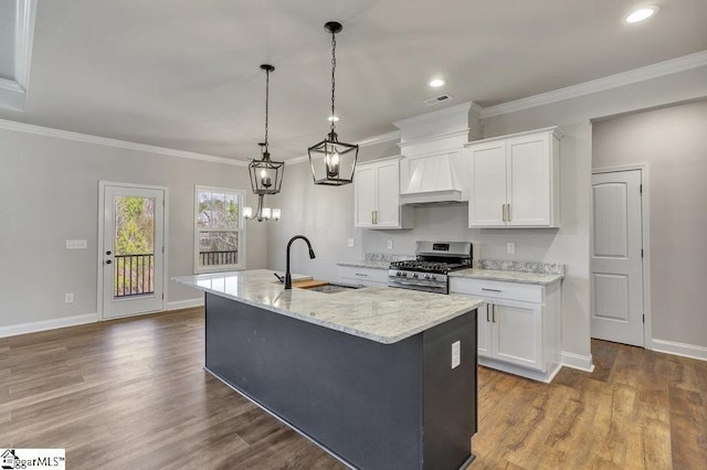 kitchen featuring custom range hood, a kitchen island with sink, stainless steel range with gas cooktop, white cabinetry, and a sink