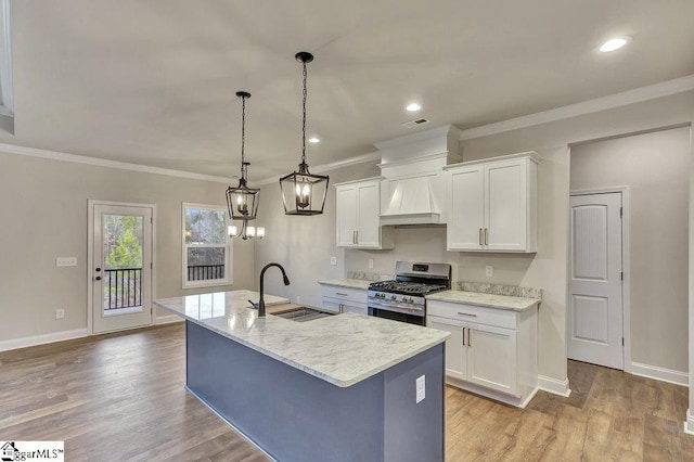 kitchen featuring stainless steel gas range, premium range hood, a center island with sink, and white cabinetry