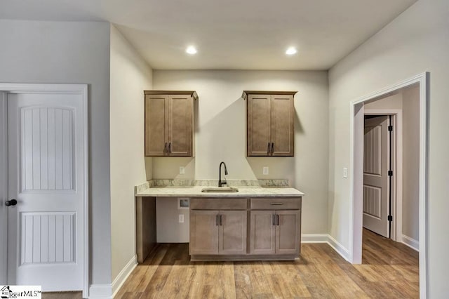 bar featuring light wood finished floors, baseboards, a sink, and recessed lighting