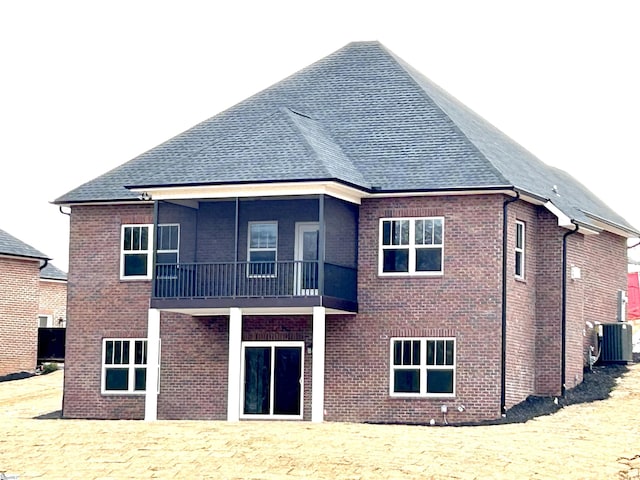 rear view of house featuring brick siding, central AC unit, a balcony, and roof with shingles