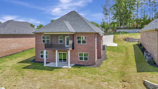 back of house with a shingled roof, a patio, a lawn, and brick siding