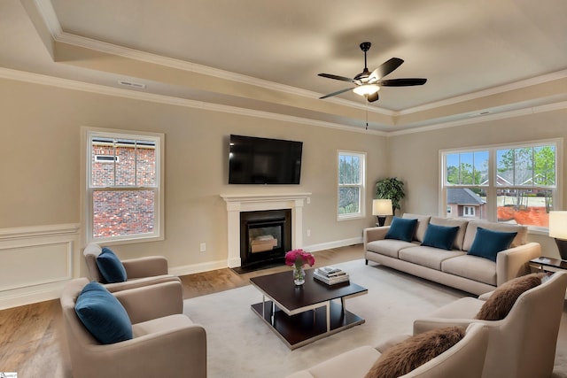 living room with light wood-style floors, a tray ceiling, visible vents, and a fireplace with flush hearth