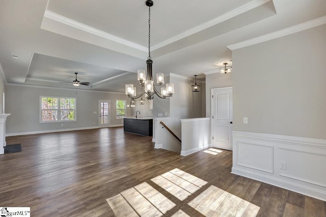 unfurnished dining area with crown molding, a tray ceiling, a decorative wall, and dark wood-style flooring