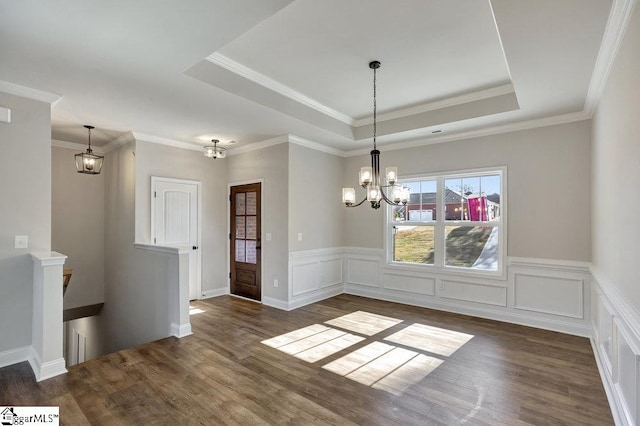 unfurnished dining area featuring a raised ceiling, dark wood-style floors, a wainscoted wall, a chandelier, and a decorative wall