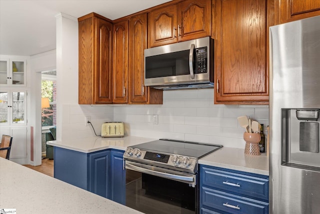 kitchen with stainless steel appliances, brown cabinetry, backsplash, and light stone countertops