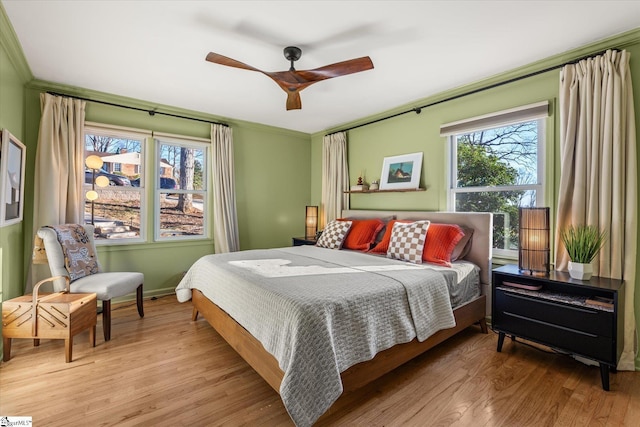 bedroom featuring light wood finished floors, ceiling fan, ornamental molding, and baseboards