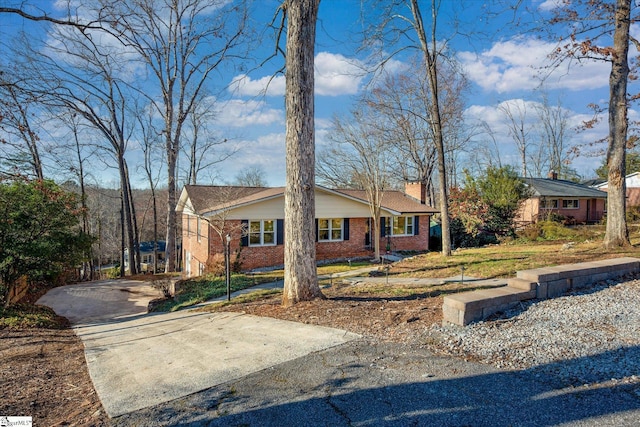 view of front of home featuring driveway, brick siding, a chimney, and a front lawn