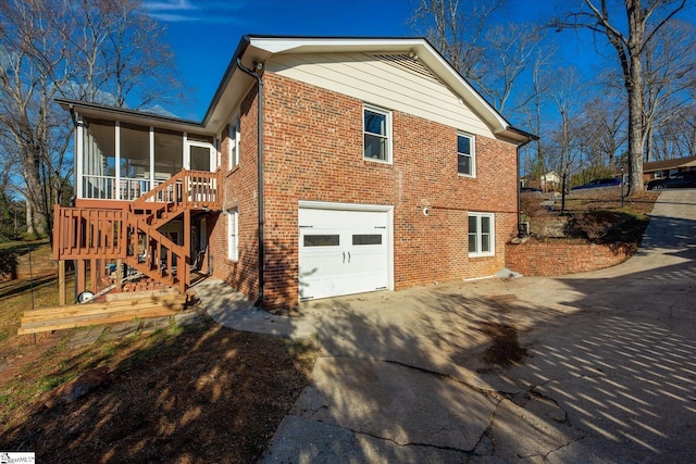 view of side of home featuring an attached garage, brick siding, a sunroom, driveway, and stairway