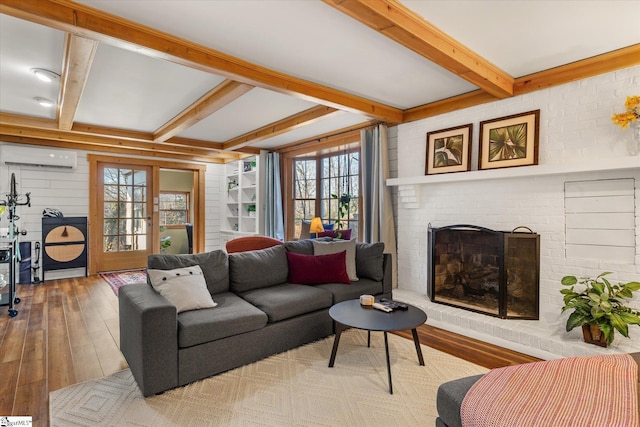 living room featuring light wood-style floors, a brick fireplace, beam ceiling, and a wall mounted AC