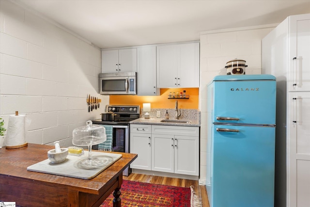 kitchen with appliances with stainless steel finishes, white cabinets, a sink, and wood finished floors