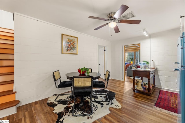 dining area with concrete block wall, a ceiling fan, and wood finished floors