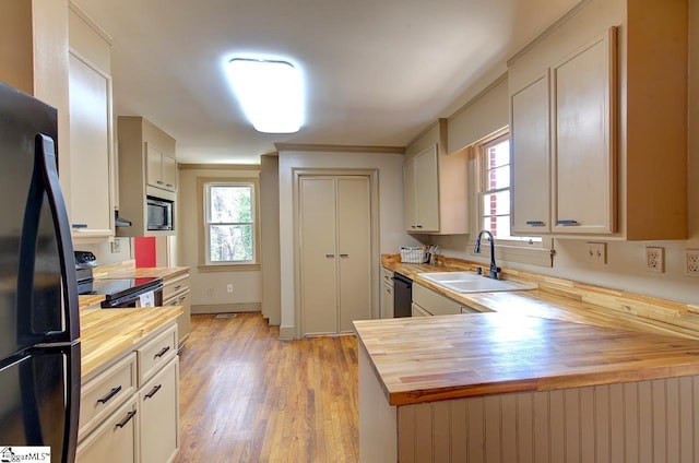 kitchen with crown molding, light wood finished floors, wooden counters, a sink, and black appliances