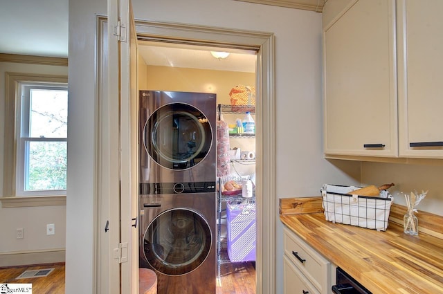 laundry room with laundry area, visible vents, stacked washer / dryer, and wood finished floors