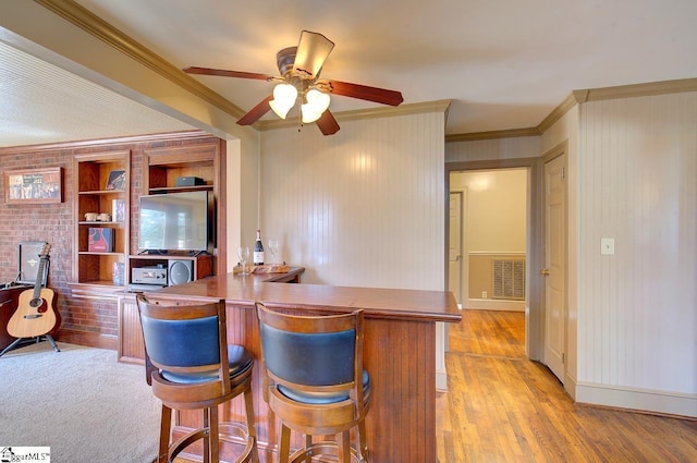 interior space featuring light wood finished floors, a peninsula, ornamental molding, and visible vents