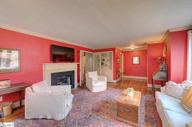 living area featuring ornamental molding, a brick fireplace, baseboards, and wood finished floors