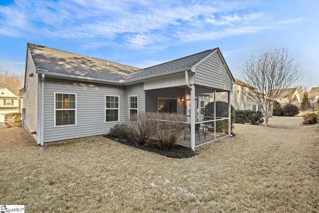 rear view of house featuring a sunroom, a shingled roof, and a lawn