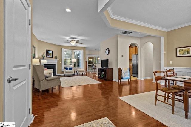 living room with visible vents, arched walkways, wood finished floors, crown molding, and a fireplace