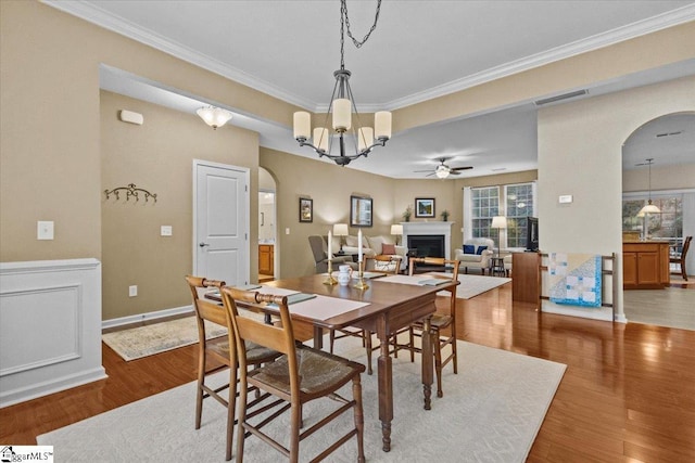 dining area with light wood finished floors, a fireplace, arched walkways, and crown molding