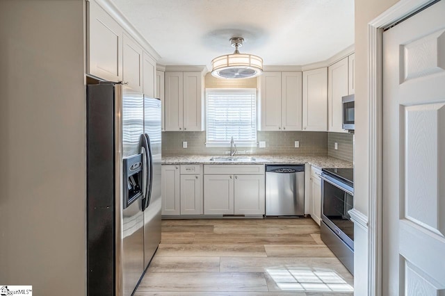 kitchen featuring a sink, appliances with stainless steel finishes, light wood-type flooring, light stone countertops, and pendant lighting