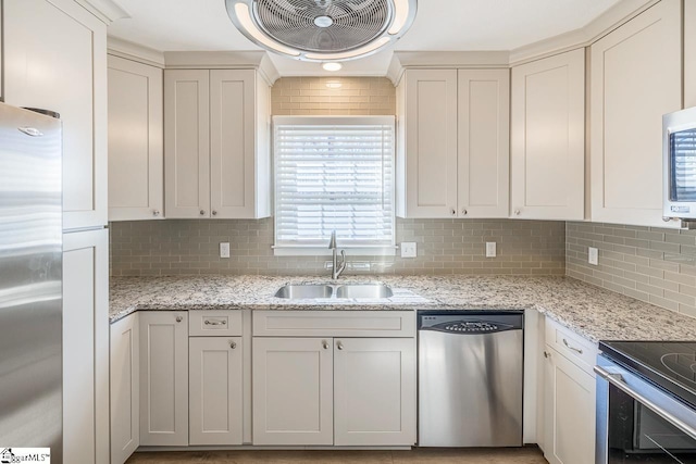 kitchen featuring stainless steel appliances, a sink, backsplash, and light stone countertops