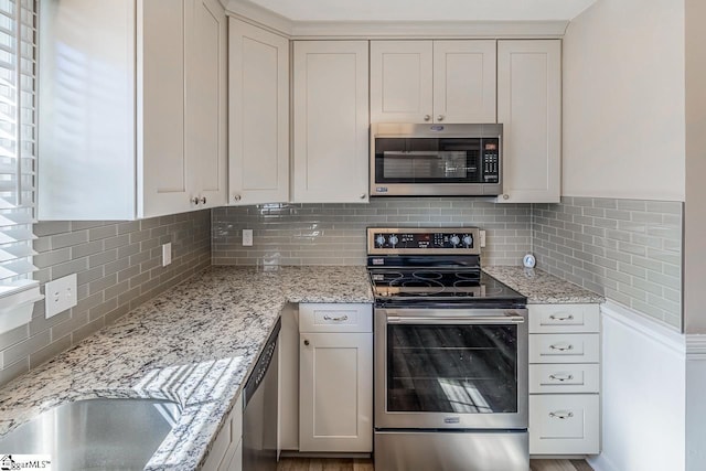 kitchen featuring white cabinets, tasteful backsplash, light stone counters, and stainless steel appliances