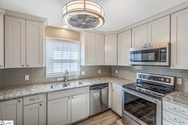 kitchen with a sink, light stone countertops, stainless steel appliances, light wood-type flooring, and backsplash