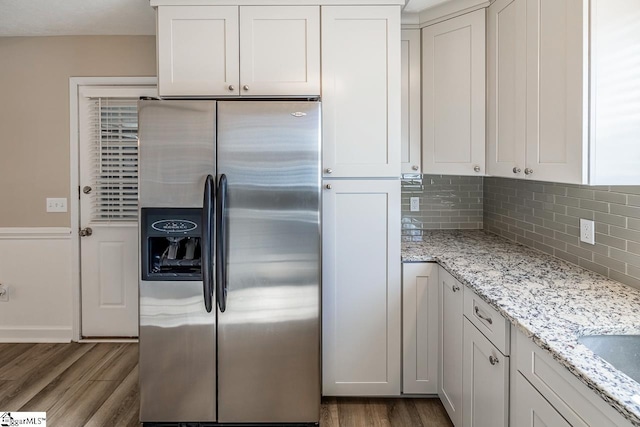 kitchen with light stone countertops, wood finished floors, stainless steel fridge, and white cabinetry