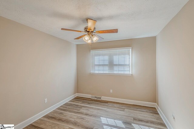 empty room with a ceiling fan, baseboards, visible vents, and light wood finished floors
