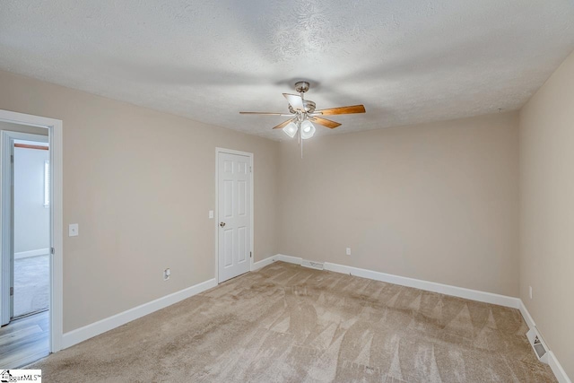 spare room with light carpet, ceiling fan, a textured ceiling, and baseboards