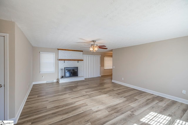 unfurnished living room with light wood finished floors, baseboards, ceiling fan, a textured ceiling, and a brick fireplace