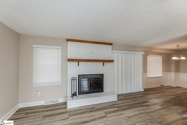 unfurnished living room with visible vents, wood finished floors, an inviting chandelier, a textured ceiling, and a brick fireplace