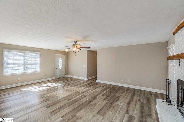 unfurnished living room featuring a textured ceiling, a fireplace, a ceiling fan, baseboards, and light wood-style floors