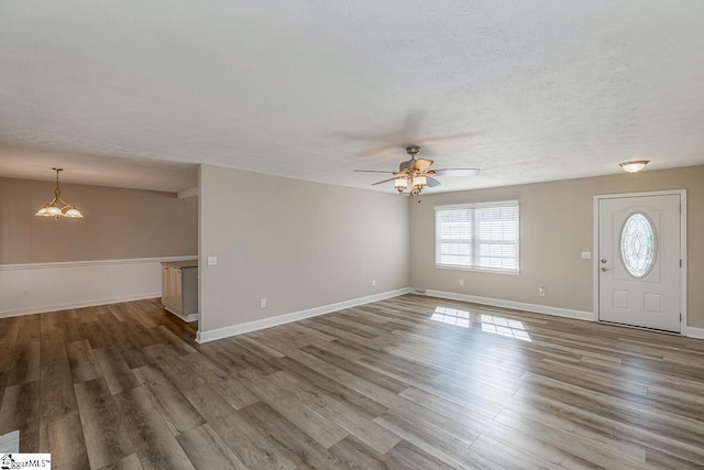 unfurnished living room featuring a textured ceiling, ceiling fan, wood finished floors, and baseboards