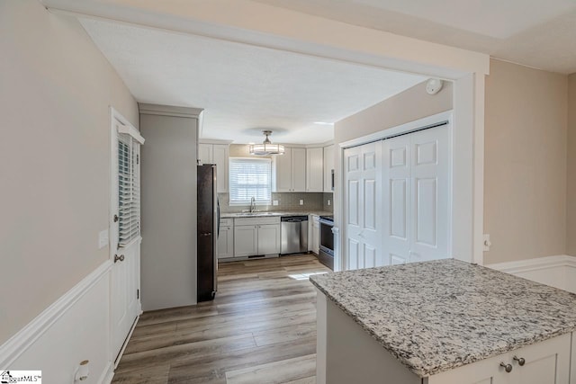 kitchen featuring light stone counters, a sink, white cabinetry, appliances with stainless steel finishes, and light wood-type flooring