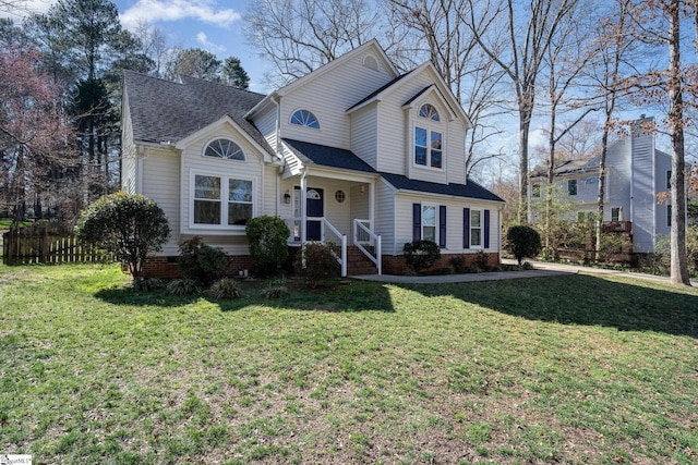 traditional home with a front lawn, a shingled roof, and fence